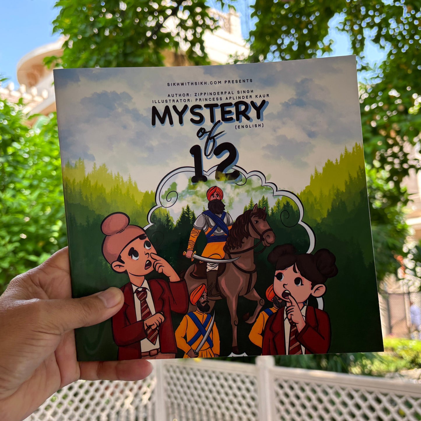 Hand holding a book titled 'Mystery of 12' with illustrations of characters and a horse against a green background.